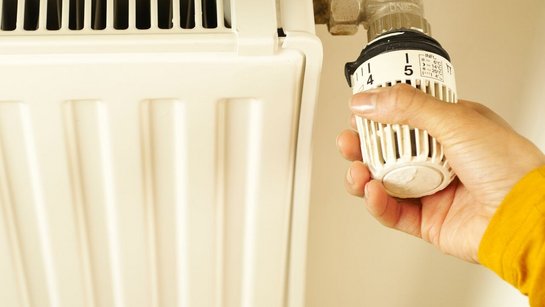 Eine Hand dreht das Thermostat an einem Heizkörper.