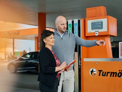 Zwei Personen besprechen einen Turmöl Standort direkt neben einer Zapfsäule.